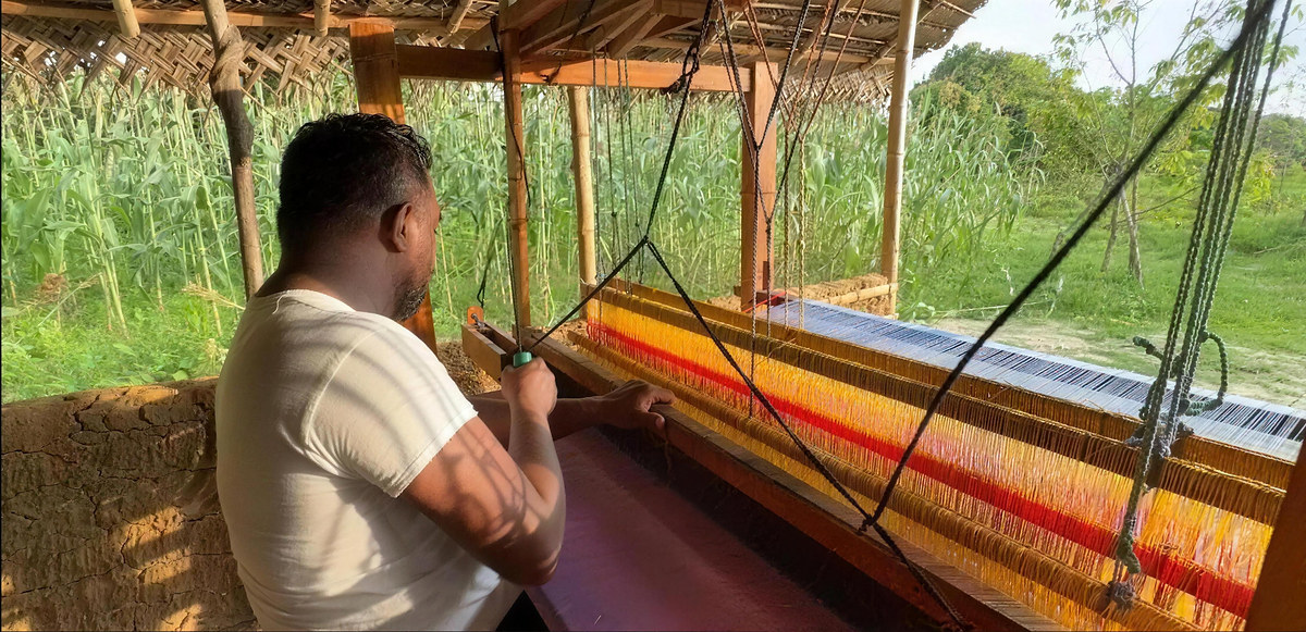 A weaver at a wooden handloom threaded with orange and red