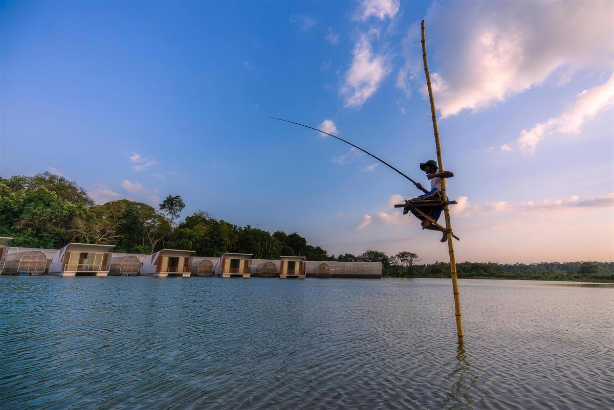 A stilt fisherman perched above the lake in front of the floating cabanas