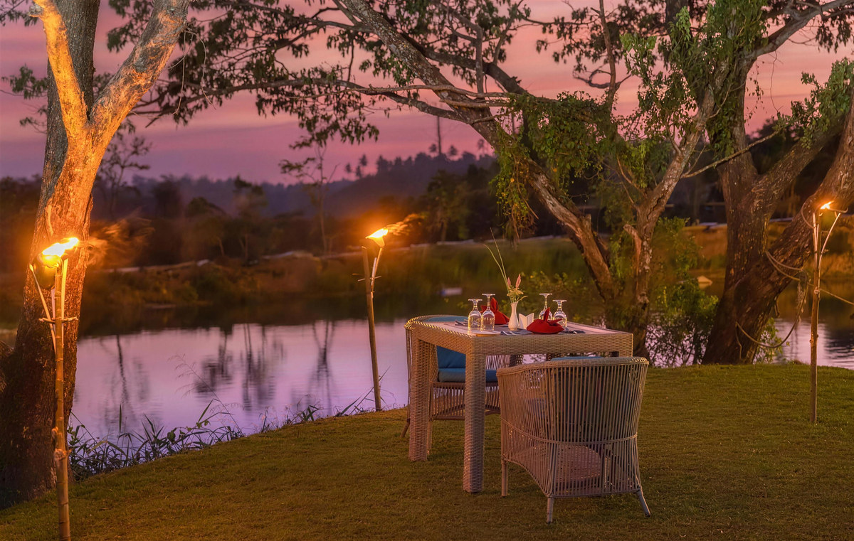 A private table for two on the lawn beside the lake, lit by torches
