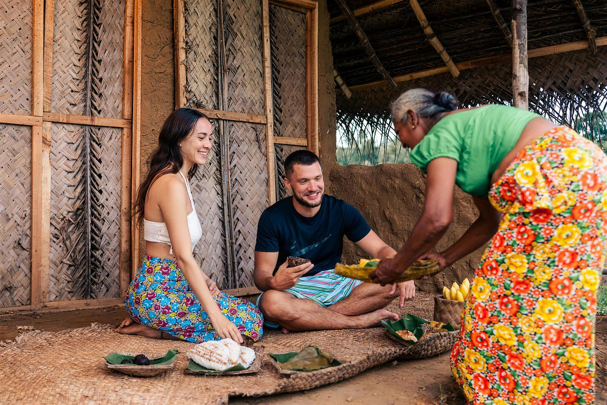 Guests seated on a mat in the village house are served rice and curry on banana leaves