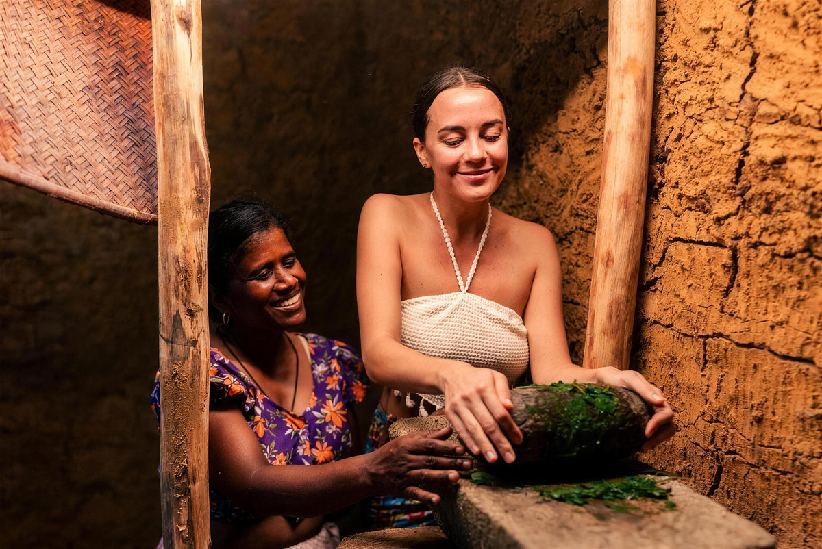 A village cook and a guest laughing over a stone mortar